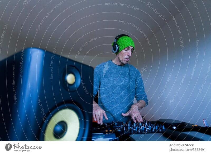 Mann spielt zu Hause am DJ-Mischpult dj Musik Konsole Mixer spielen Klang Gerät mischen Beanie heimwärts Audio Regler Schaltfläche unterhalten Aufzeichnen