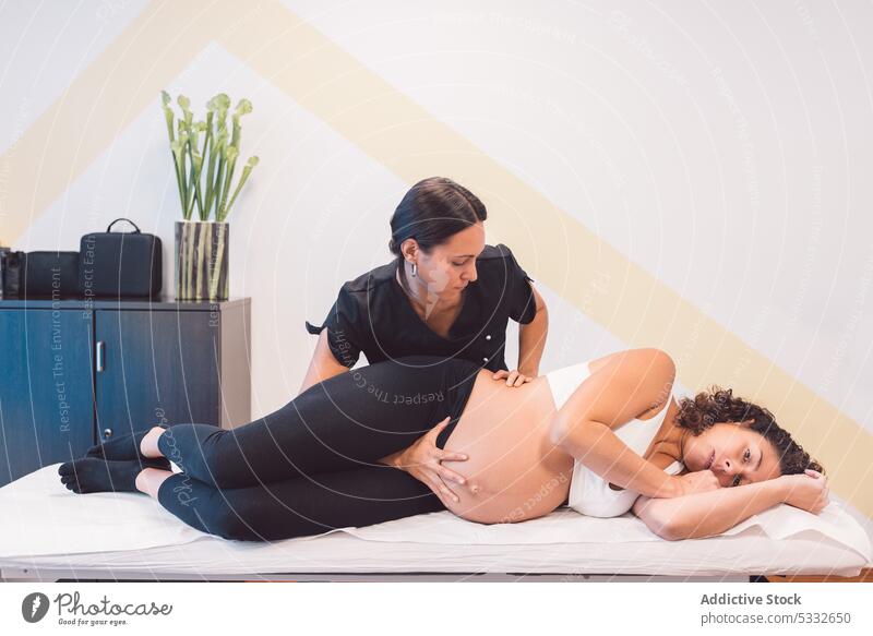 Therapeutin massiert den Bauch einer schwangeren Kundin Frau Osteopath geduldig Baby Erleichterung mütterlich Klinik Unterleib pränatal Hilfsbereitschaft Magen