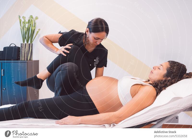 Masseurin massiert schwangere Kundin auf einer Bank Frau geduldig Osteopath Therapie Rehabilitation Physiotherapie Klinik Bein angehoben Leckerbissen Massage
