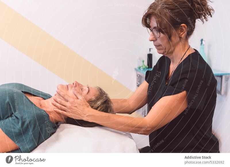 Masseurin bei der Gesichtsmassage eines Kunden Frau Massage Physiotherapeutin Osteopath geduldig Kopf Verfahren Therapie Therapeut Lügen Rehabilitation