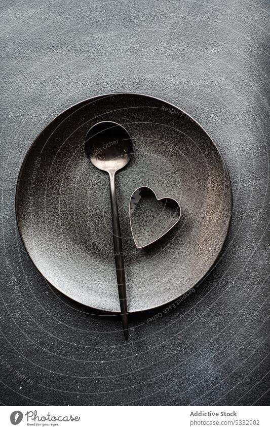 Minimalistisches Tischset in schwarzer Farbe mit Löffel und Herz Hintergrund Keramik Beton Keks Besteck Kutter Abendessen Essgeschirr Essen Lebensmittel