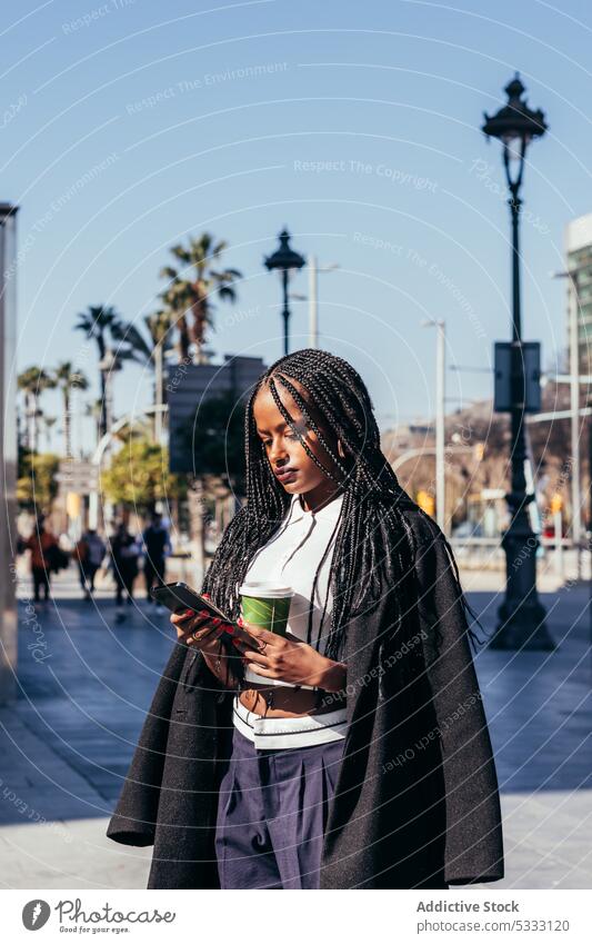 Schwarze Frau mit Smartphone auf der Straße Kaffee Freude trinken heiter Browsen Imbissbude positiv Afroamerikaner schwarz ethnisch Tasse Funktelefon Afro-Zöpfe