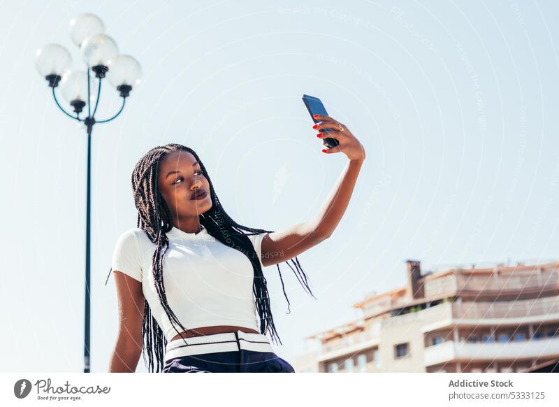 Schwarze Frau macht Selfie mit Smartphone benutzend Selbstportrait Straße Gerät Mobile Funktelefon fotografieren Großstadt Bank lässig Afroamerikaner ethnisch