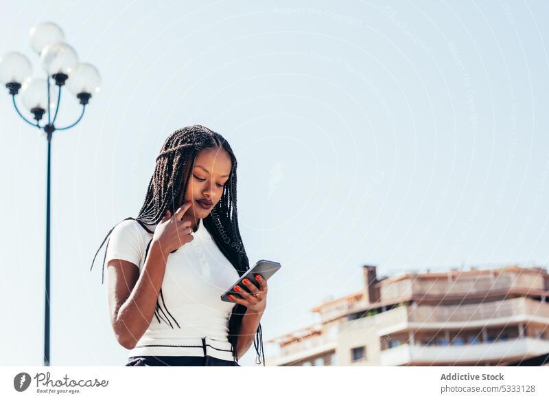 Schwarze Frau benutzt Smartphone auf der Straße benutzend cool Browsen positiv Nachricht Surfen Funktelefon heiter modern ethnisch schwarz Afroamerikaner lässig