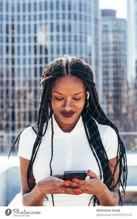 Fröhliche schwarze Frau benutzt Smartphone auf der Straße benutzend cool Lächeln Browsen positiv Nachricht Glück Surfen Funktelefon heiter modern ethnisch