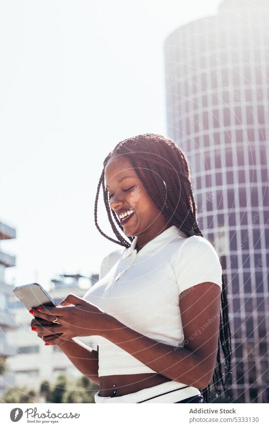 Fröhliche schwarze Frau benutzt Smartphone auf der Straße benutzend cool Lächeln Browsen positiv Nachricht Glück Surfen Funktelefon heiter modern ethnisch