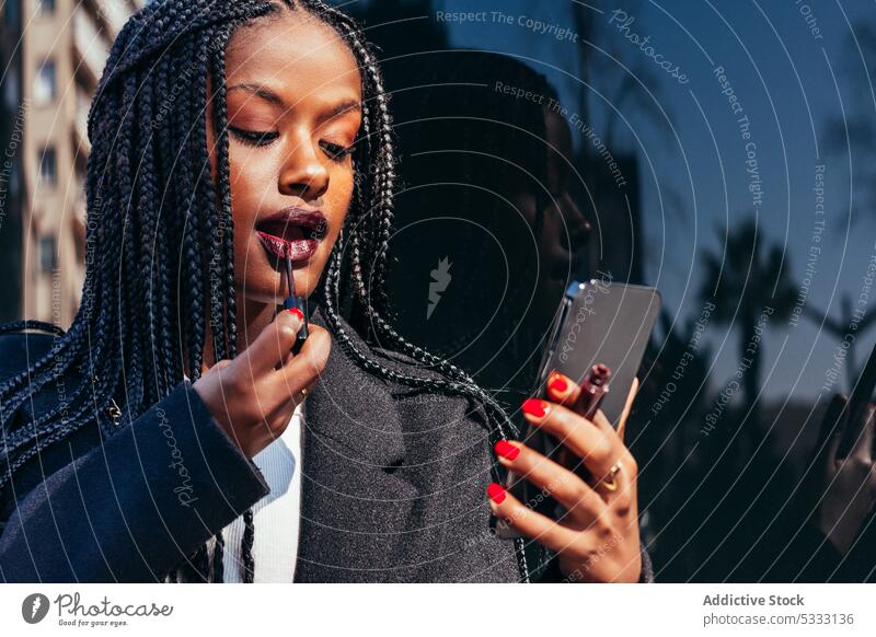 Schwarze Frau trägt auf der Straße Lippenstift auf Smartphone bewerben Make-up benutzend Geflecht Gerät Mobile Gesicht Afroamerikaner ethnisch schwarz Afro-Look