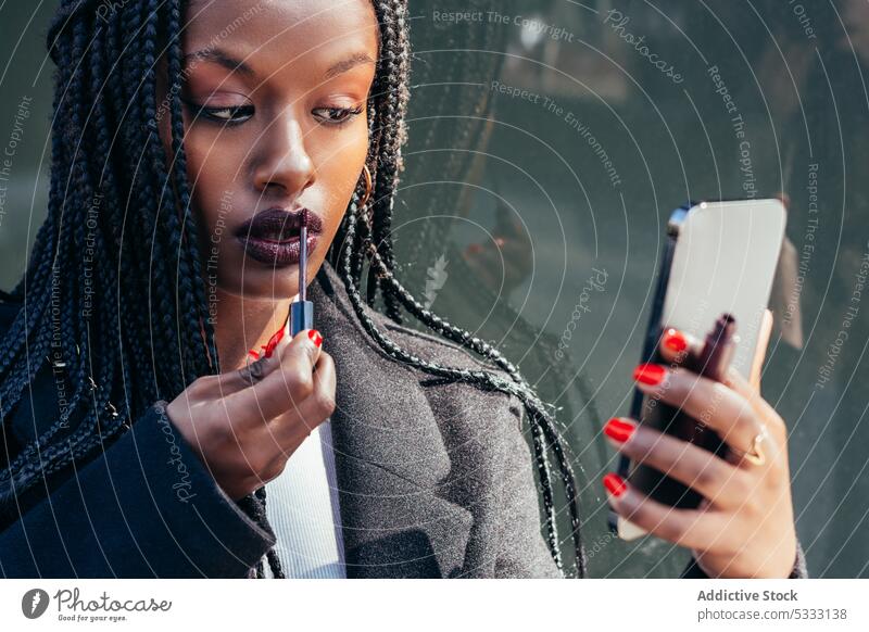 Schwarze Frau trägt auf der Straße Lippenstift auf Smartphone bewerben Make-up benutzend Geflecht Gerät Mobile Gesicht Afroamerikaner ethnisch schwarz Afro-Look