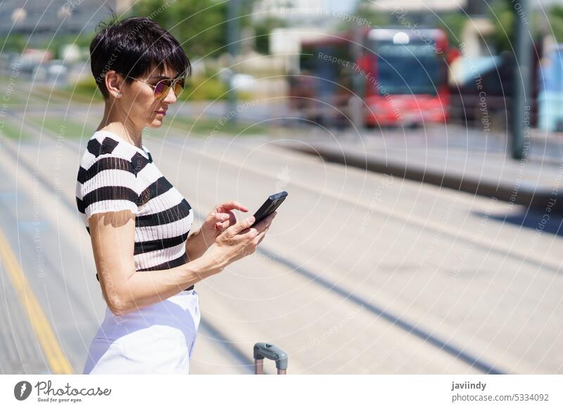 Seriöse Frau, die in der Innenstadt eine SMS auf ihrem Smartphone schreibt benutzend Fokus Koffer Tourist Sommer Podest ernst warten Feiertag reisen prüfen