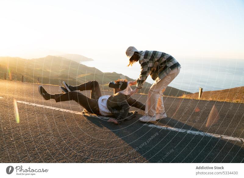 Mann stürzt in der Nähe seiner Freundin auf der Straße vom Skateboard Paar VR Schutzbrille fallen Zusammensein Partnerschaft Skater Sonnenuntergang MEER