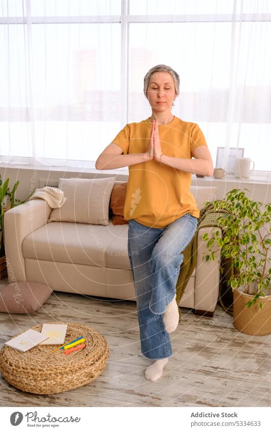 Erwachsene Frau meditiert zu Hause bei Tageslicht meditieren Yoga Gleichgewicht üben Übung Wellness Training Sofa Pflanze beweglich Chemotherapie Überlebender