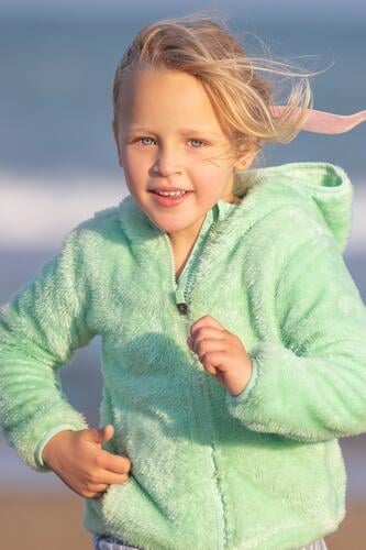 Ein 5-jähriges Mädchen in einer grünen Jacke läuft Kind Kindheit blond 5 Jahre alt Strand MEER Sand Meer Küste vertikal jung Auge blau Feiertag Lifestyle Himmel