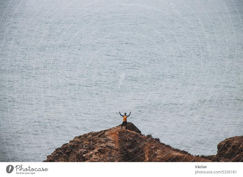 Ein abenteuerlustiger Mann steht am Rande einer Klippe und genießt die Aussicht auf die Atlantikküste in der Region Odemira im Südwesten Portugals. Wanderung durch die Rota Vicentina