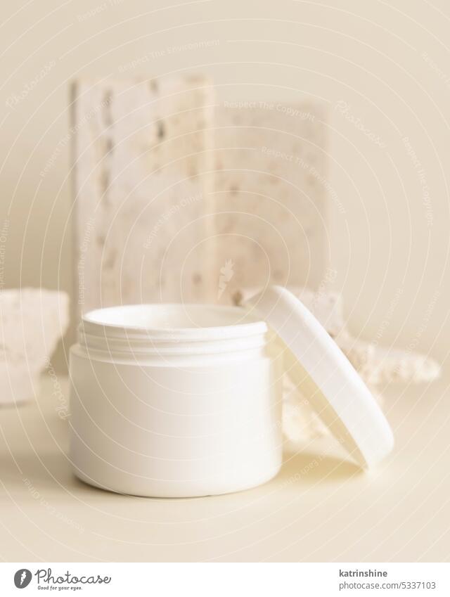 Geöffnetes weißes Cremetöpfchen mit Deckel in der Nähe von Biegesteinen in Großaufnahme. Kosmetisches Mockup Glas Kosmetik Attrappe Sahne aufgeklappt beige