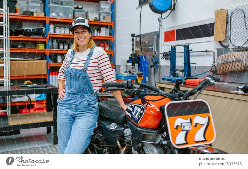 Mechanikerin stehend auf Motorradfabrik Frau Fabrik Werkstatt Lächeln freundlich Fröhlichkeit Glück Blick Fotokamera Garage Beruf Arbeiter Stehen Porträt