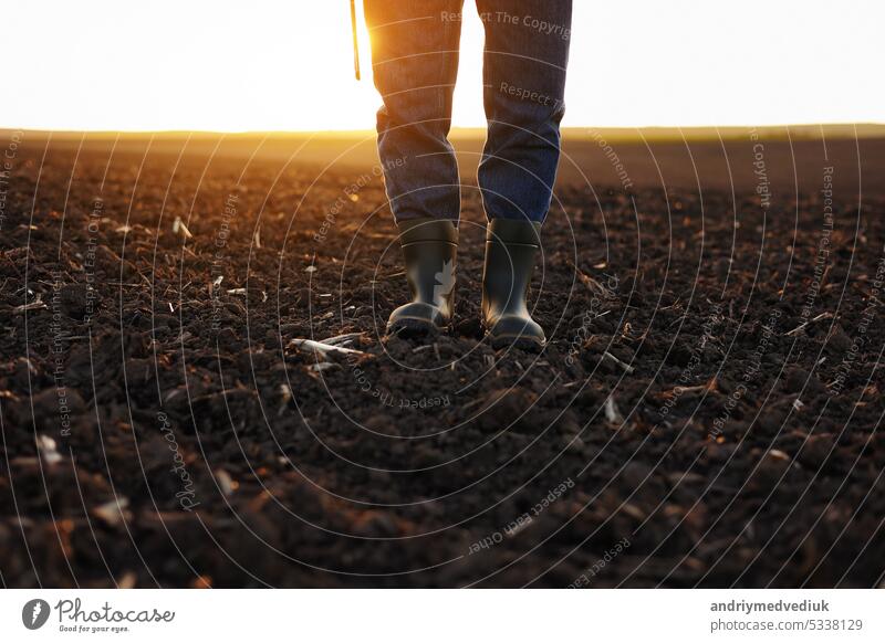 Landwirtschaft. Cropped Schuss der Ansicht Geschäftsmann Landwirt in Gummistiefeln geht entlang gepflügten Feld mit digitalen Tablet. Agronom überprüft und analysiert fruchtbaren Boden auf Sonnenaufgang. Agribusiness.