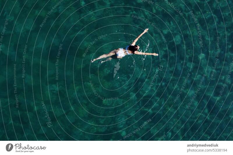 Blick von oben auf eine Frau, die im Meer schwimmt. Luftaufnahme von oben eines jungen Mädchens im weißen Badeanzug, das auf der Wasseroberfläche im kristallklaren türkisfarbenen Meer schwimmt. Urlaub im Paradies. Ozean entspannen, Reisen und Urlaub