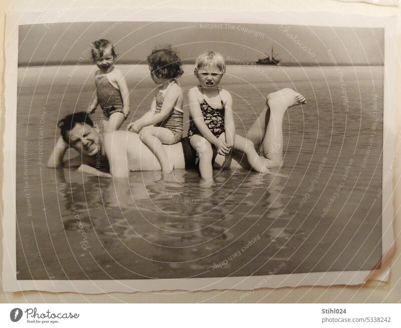 Kinder sitzen auf liegendem Vater am Sandstrand - Vater mit Kindern Urlaub am Strand baden entspannt Wasser Nordsee 50er JAhre schwarzweiß Erholung