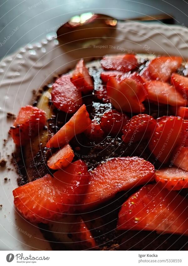 Nahaufnahme eines vollen Tellers mit Porridge und frisch geschnittenen Erdbeeren, bestreut mit Kakaopulver, auf einem schwarzen Tisch mit goldenem Löffel.
