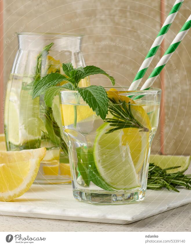 Limonade in einem transparenten Glas mit Zitrone, Limette, Rosmarinzweigen und Minzblättern auf weißem Hintergrund Kalk trinken Cocktail Erfrischung Frucht Eis