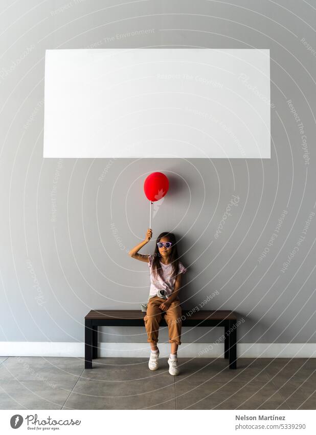 Ein Mädchen sitzt allein auf einer Bank und hält einen Globus Sitzen vereinzelt rot Luftballon leer weiß Holzplatte Einsamkeit Kontemplation