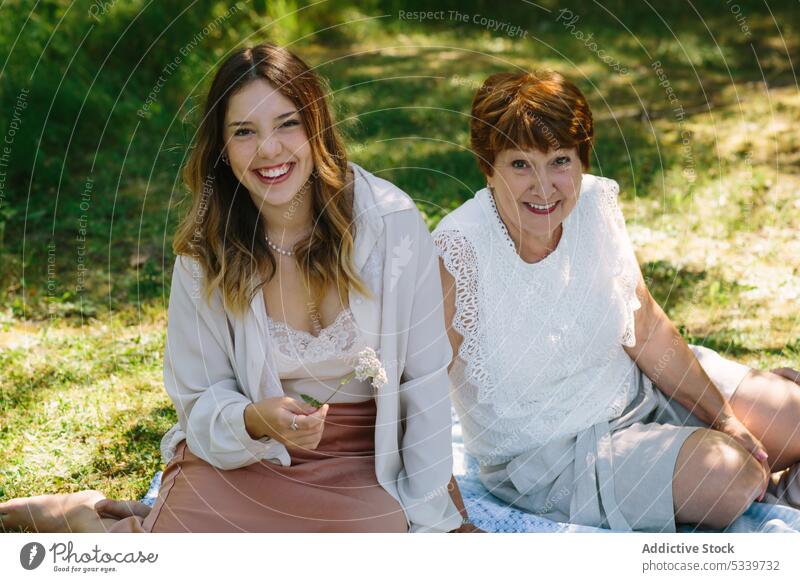 Fröhliche Frauen schauen in die Kamera und lächeln auf dem Rasen Enkelin Sommer Picknick Großmutter Park Lächeln Zusammensein Glück ruhen Partnerschaft Senior
