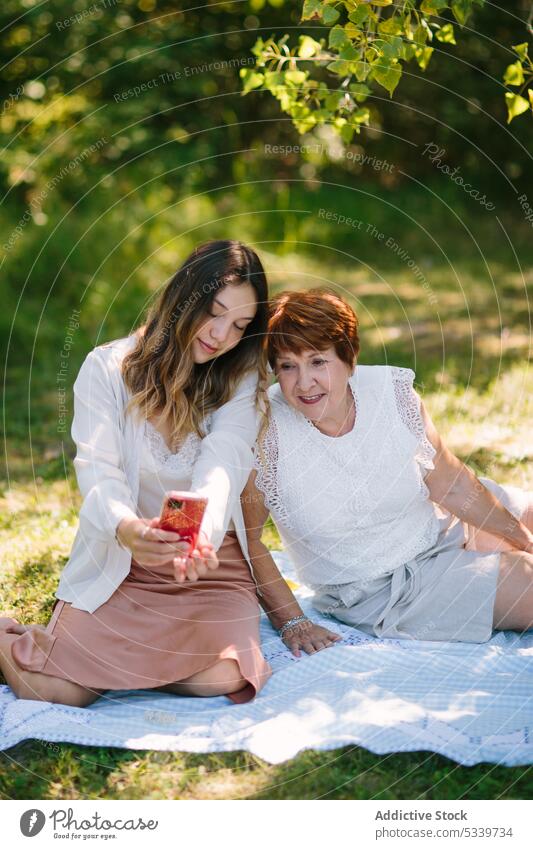 Inhalt Teenager-Mädchen mit Smartphone in der Nähe einer älteren Frau auf einer Picknick-Decke Enkelin Zusammensein teilen Park Großmutter soziale Netzwerke