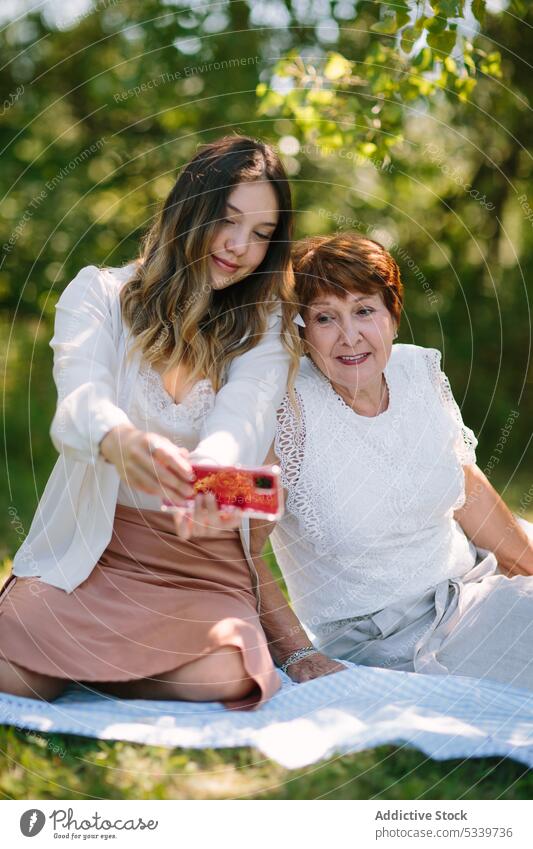 Inhalt Teenager-Mädchen mit Smartphone in der Nähe einer älteren Frau auf einer Picknick-Decke Enkelin Zusammensein teilen Park Großmutter soziale Netzwerke