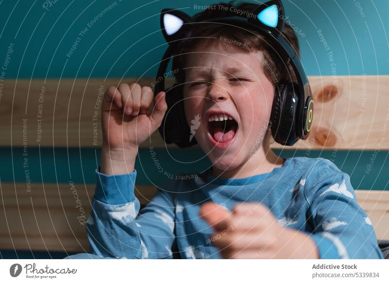 Aufgeregtes Kind, das mit Kopfhörern Musik hört singen Augen geschlossen aufgeregt schreien zuhören Schreien Sie die Faust ballen Drahtlos Nacht sorgenfrei