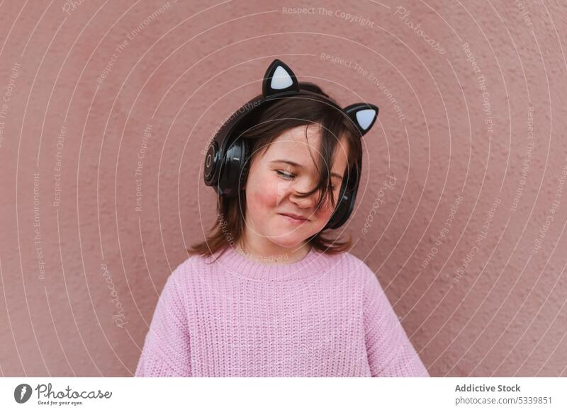 Fröhliches Mädchen mit Kopfhörern vor bräunlich-rosa Wand Lächeln zuhören Musik Kind Porträt Glück niedlich Apparatur bezaubernd Straße Klang Audio heimwärts