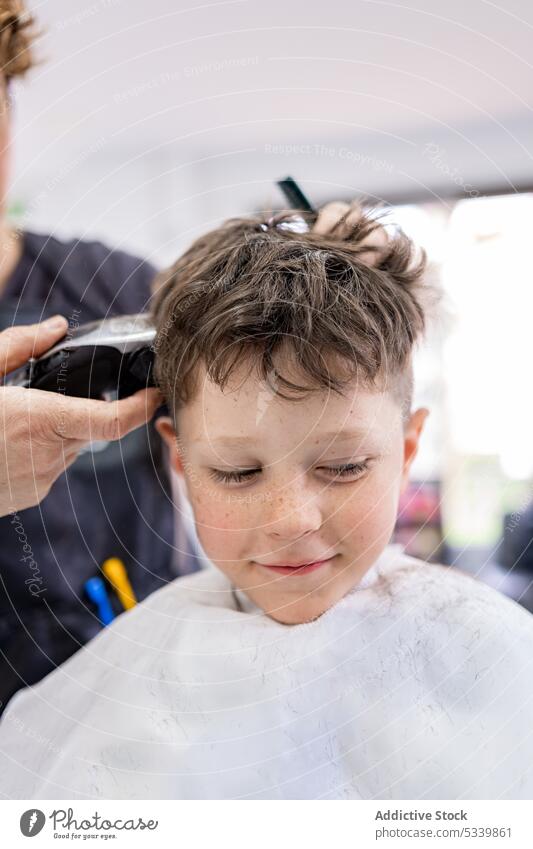 Anonymer Friseur, der einem Kind die Haare schneidet Klient Stuhl Frisur Haarschnitt Gewebe Atelier Komfort Windstille Kamm Salon Pflege Maschine Gerät Stil