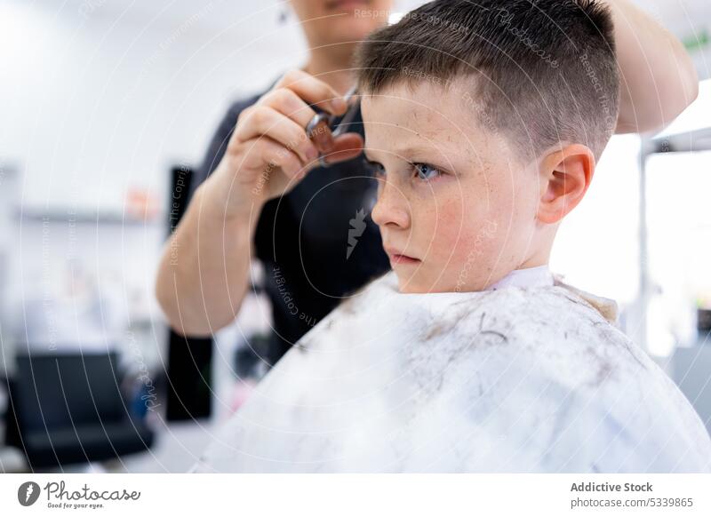Unbekannter Friseur, der einem Jungen im Salon die Haare schneidet Kind Haarschnitt Frisur Klient Kamm Schere professionell Kindheit Stil Arbeit Beruf Prozess