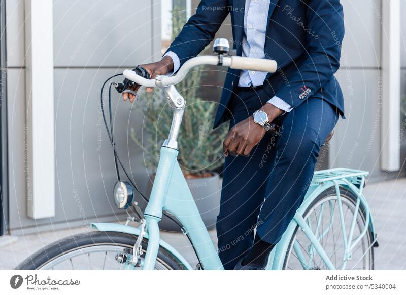Anonymer schwarzer Geschäftsmann fährt Fahrrad auf der Straße Mitfahrgelegenheit Unternehmer Arbeit Gebäude Afroamerikaner männlich Mann gut gekleidet zuschauen