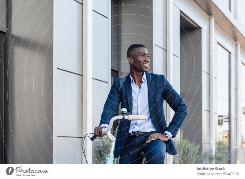 Glücklicher schwarzer Geschäftsmann fährt Fahrrad auf der Straße Mitfahrgelegenheit Unternehmer Arbeit Lächeln heiter positiv Gebäude Afroamerikaner männlich