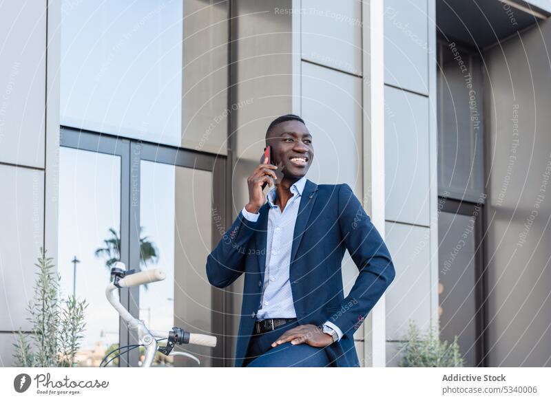 Glücklicher schwarzer Geschäftsmann, der mit seinem Smartphone spricht, während er Fahrrad fährt Telefonanruf Mitfahrgelegenheit Gespräch diskutieren reden