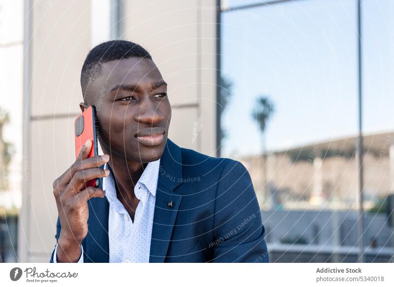 Schwarzer Geschäftsmann spricht in der Nähe eines Gebäudes mit seinem Smartphone Mann Mitarbeiter reden sprechen Gespräch Büro Kommunizieren Telefon benutzend