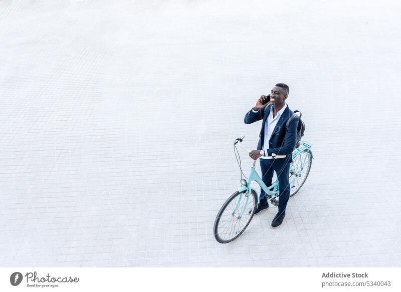 Schwarzer Geschäftsmann mit Fahrrad und Rucksack im Gespräch am Telefon Mann Mitfahrgelegenheit reden Lächeln heiter sprechen Kommunizieren positiv Smartphone