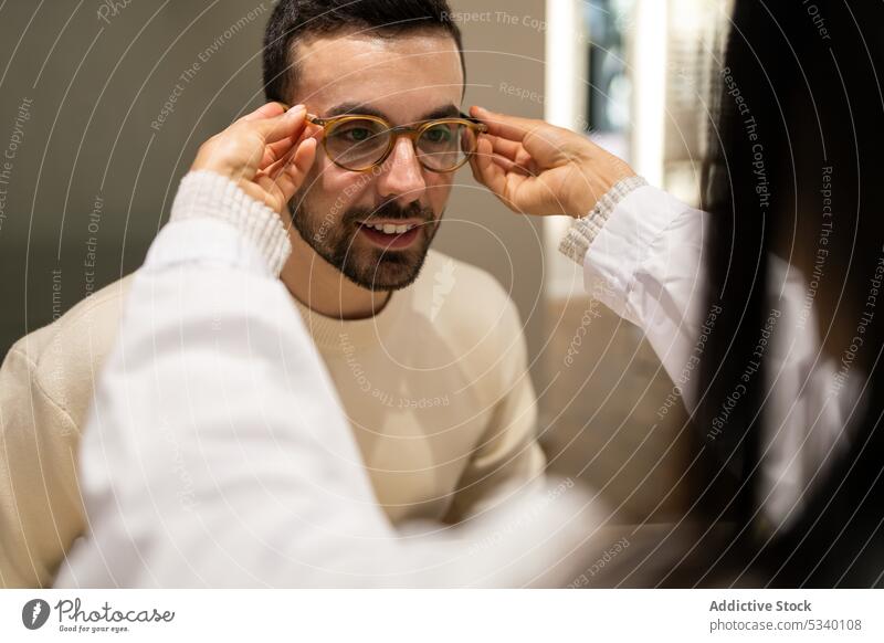 Anonyme Augenärztin, die einem männlichen Kunden hilft, eine Brille zu tragen Mann wählen Laden optisch Lächeln Ophthalmologe Augenlicht Sehvermögen Werkstatt