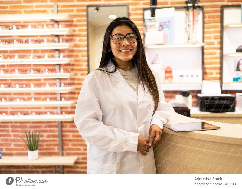 Glückliche Augenärztin in Uniform und mit Brille schaut in die Kamera Frau professionell Okular optisch Job heiter Lächeln Ophthalmologe Arzt positiv Arbeit