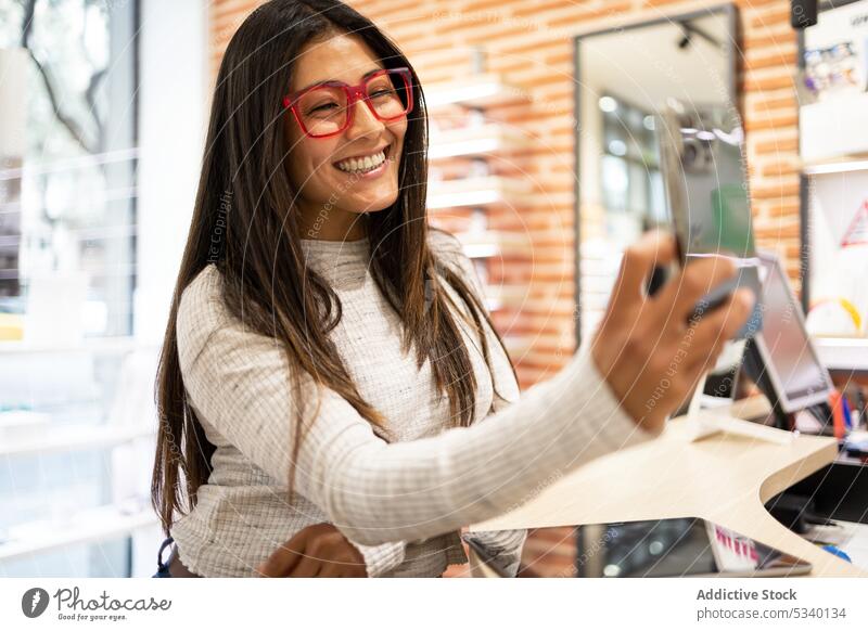 Glückliche Frau mit Brille, die ein Selfie in einem optischen Geschäft macht Kunde kaufen Smartphone benutzend Regal wählen heiter Laden Mobile Telefon Lächeln