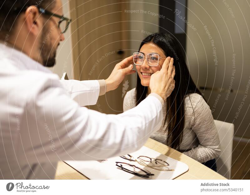 Glückliche Frau wählt in einem Optikergeschäft eine Brille aus Kunde anprobieren neu optisch Laden Assistent wählen Lächeln heiter Wahl Werkstatt jung