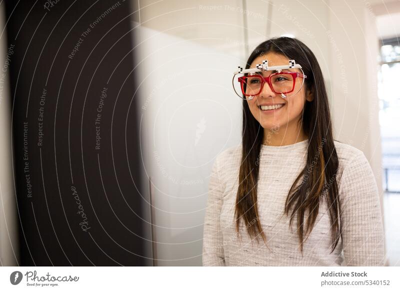 Lächelnde Frau mit Probebrille in einem Optikgeschäft Kunde anprobieren Rahmen Brille Sehvermögen prüfen optisch Laden Ophthalmologie Glück wählen jung