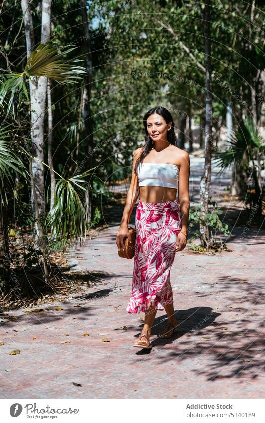 Zufriedene Frau, die auf einem Weg zwischen tropischen Palmen spazieren geht Spaziergang Handfläche Sommer exotisch Natur Stil Straße ruhig jung Windstille