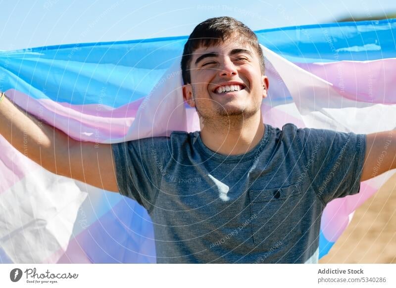 Fröhlicher Schwuler mit Transgender-Flagge Mann schwul Stolz Fahne feiern Feiertag aufgeregt Lächeln Strand männlich lgbt lgbtq Homosexualität transsexuell