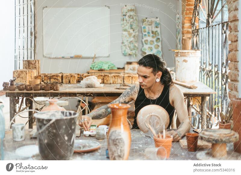 Mann malt auf einer Tonplatte in einer Werkstatt Künstler Farbe Kunsthandwerker zeichnen Ornament kreativ Tisch bewerben Töpferwaren Handwerk Fähigkeit