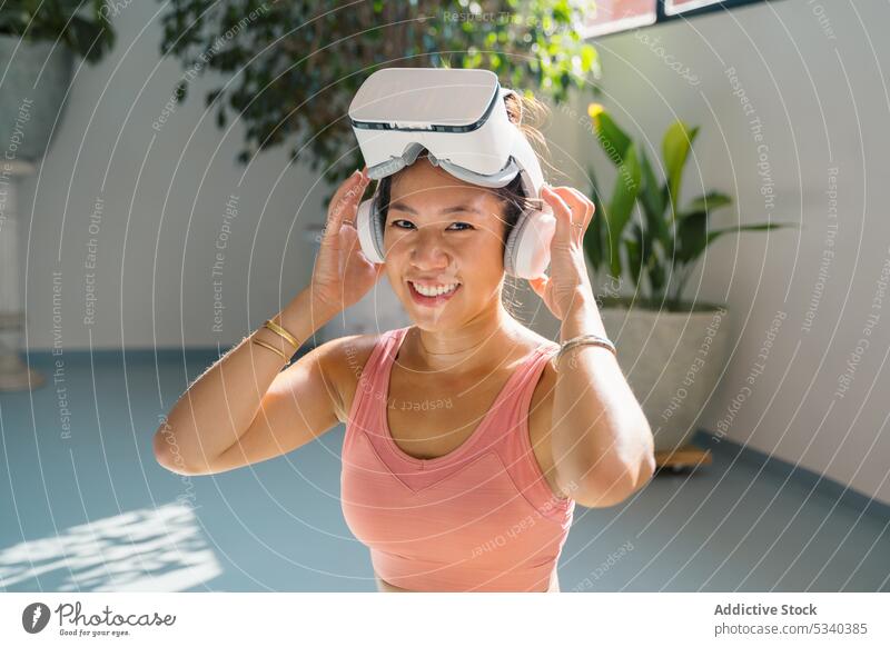 Lächelnde Frau in VR-Headset auf Yogamatte padmasana asiatisch Chinesisch ethnisch Lotus-Pose Virtuelle Realität Schutzbrille heiter Asana üben Wellness