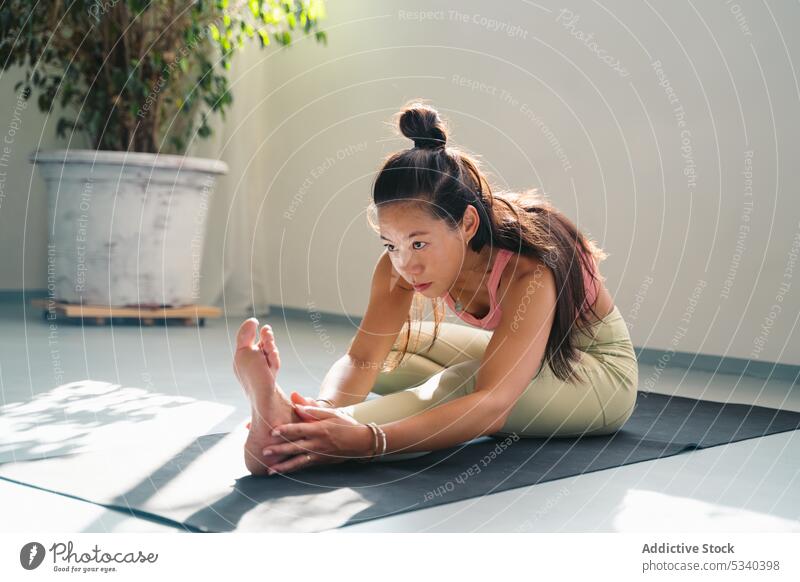 Fokussierte asiatische Frau, die sich im Sitzen in der dreigliedrigen Vorwärtsbeuge dehnt Yoga Dehnung Asana üben Konzentration beweglich Achtsamkeit jung