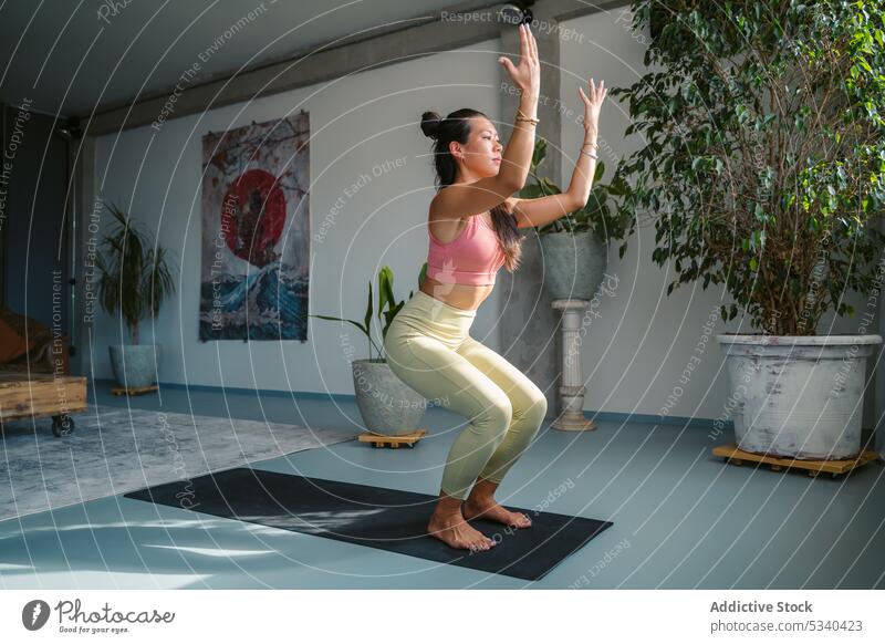 Schlanke asiatische Frau übt Göttin-Pose mit Kaktus-Armen auf Matte Yoga Asana beweglich Achtsamkeit üben Konzentration Göttin mit Kaktusarmen Dehnung