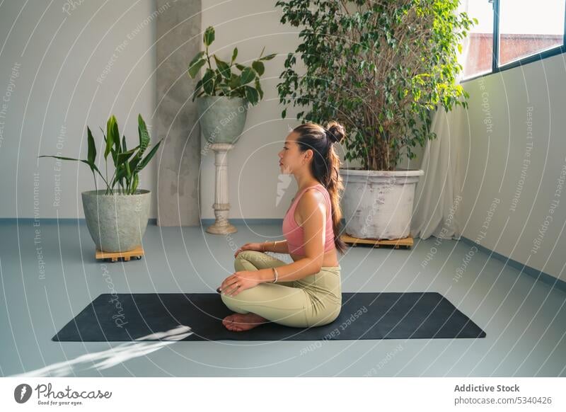 Asiatische Frau in Lotus-Pose auf Matte im Studio Yoga padmasana meditieren Achtsamkeit Zen friedlich Stressabbau üben jung Sportkleidung Asana ethnisch
