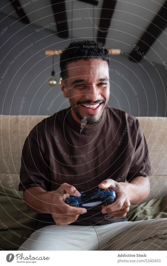 Fröhlicher ethnischer Mann spielt ein Videospiel auf dem Bett spielen Joystick Gamepad Lächeln Wochenende Glück Spieler heimwärts Afroamerikaner jung heiter